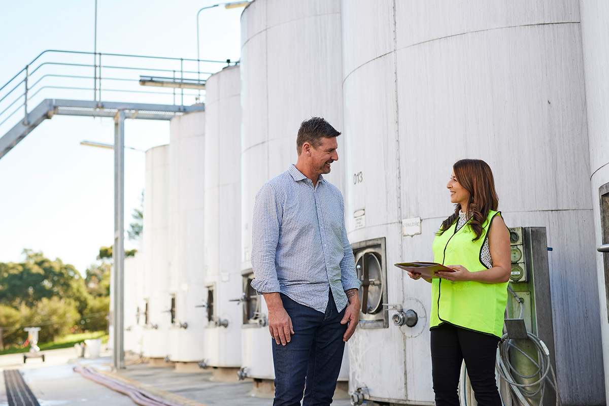 Female case manager and male winemaker talking in front of wine tanks